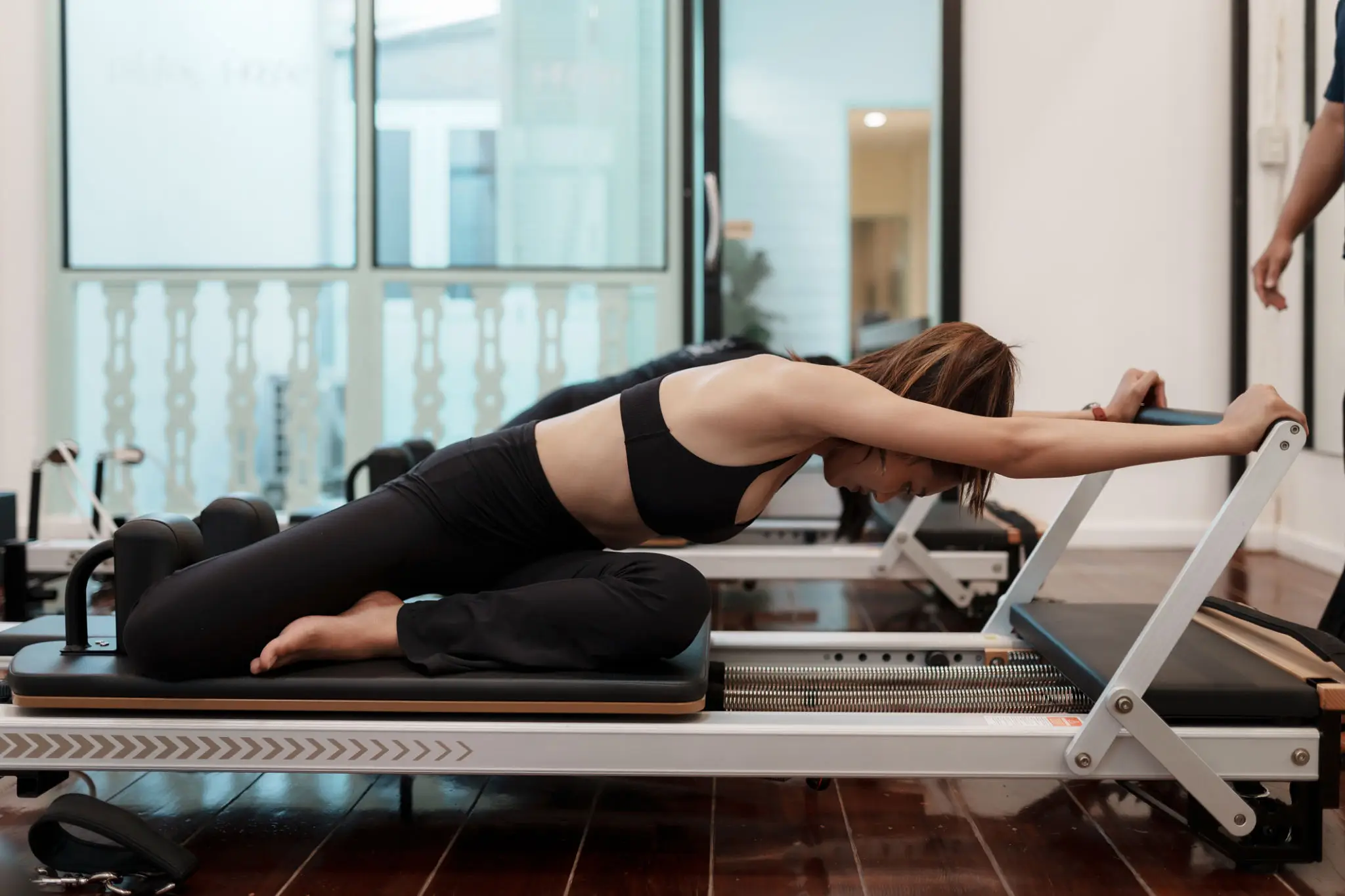 Woman stretching on a Pilates reformer machine indoors.
