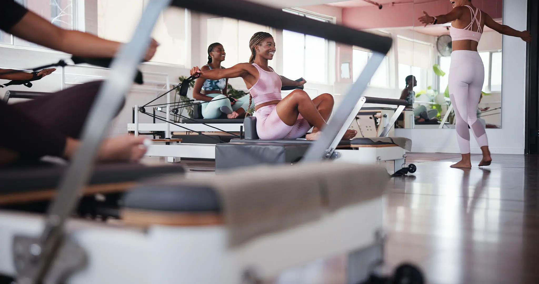 Women exercising on Pilates reformer machines in a bright studio.
