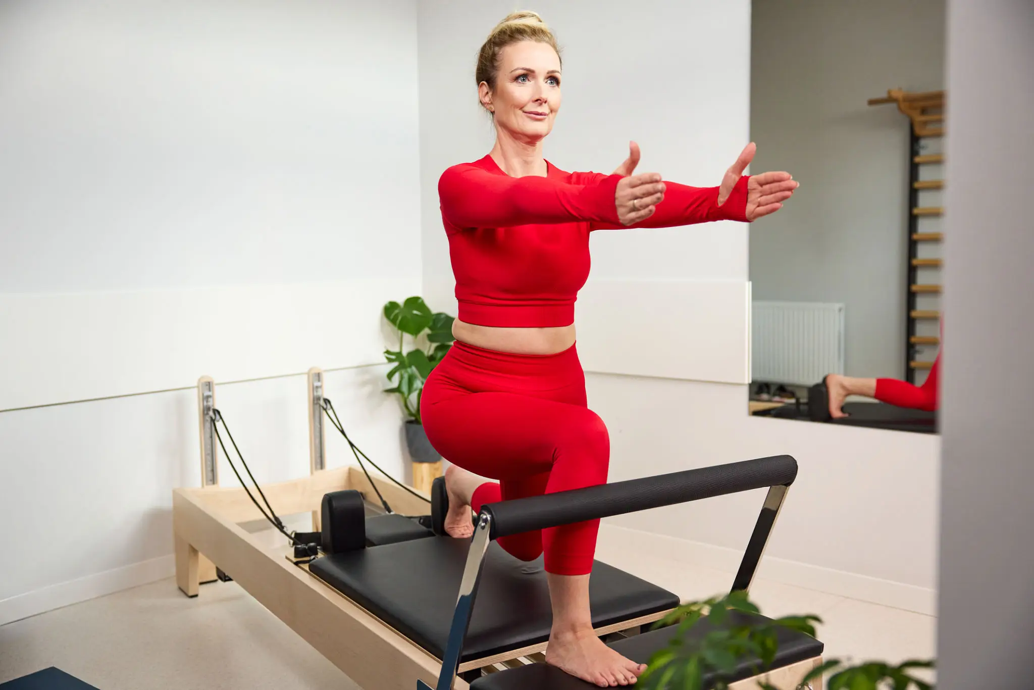 Woman exercising on Pilates reformer machine in red workout outfit.