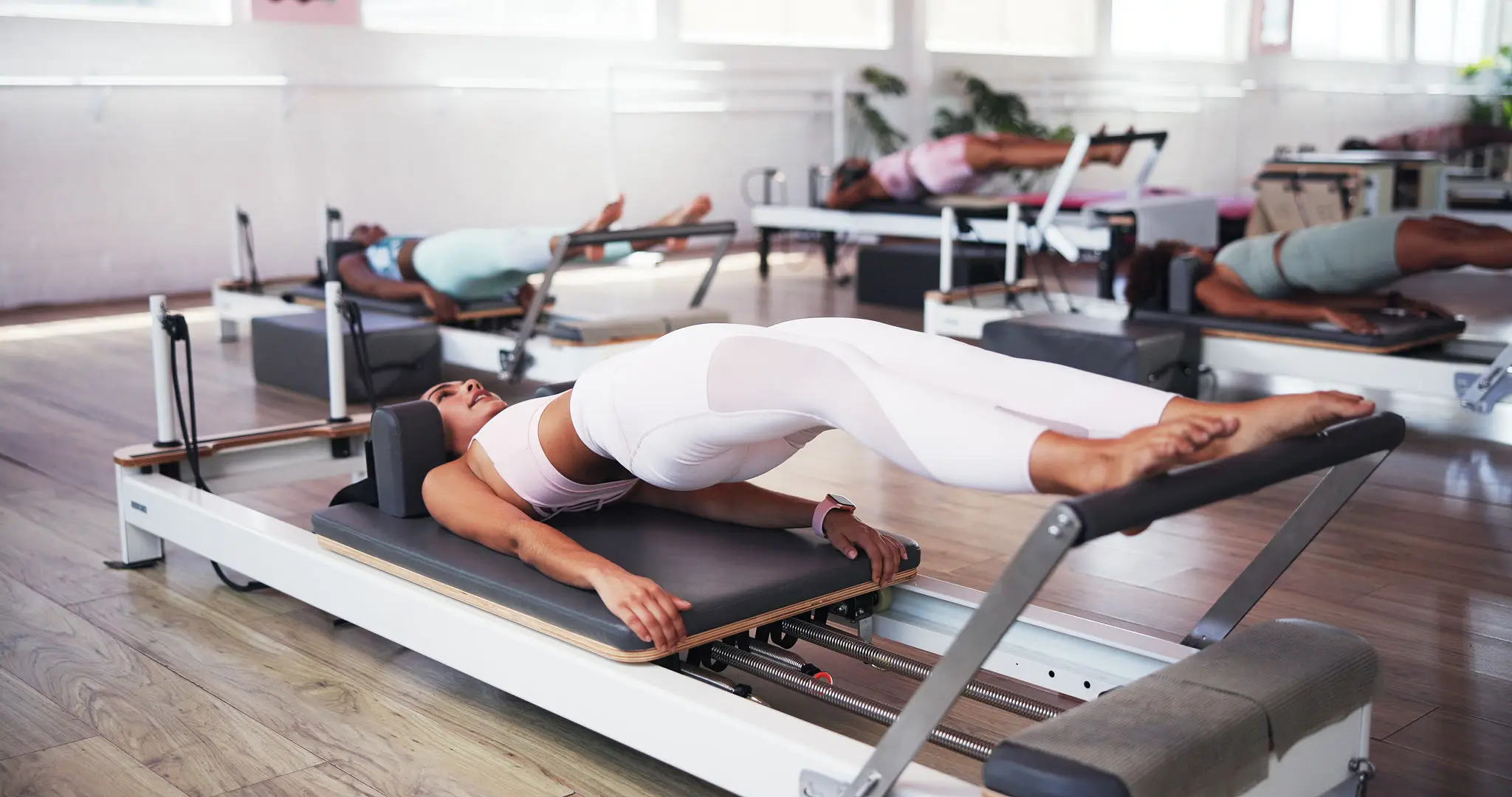 Woman performing Pilates exercise on reformer machine.