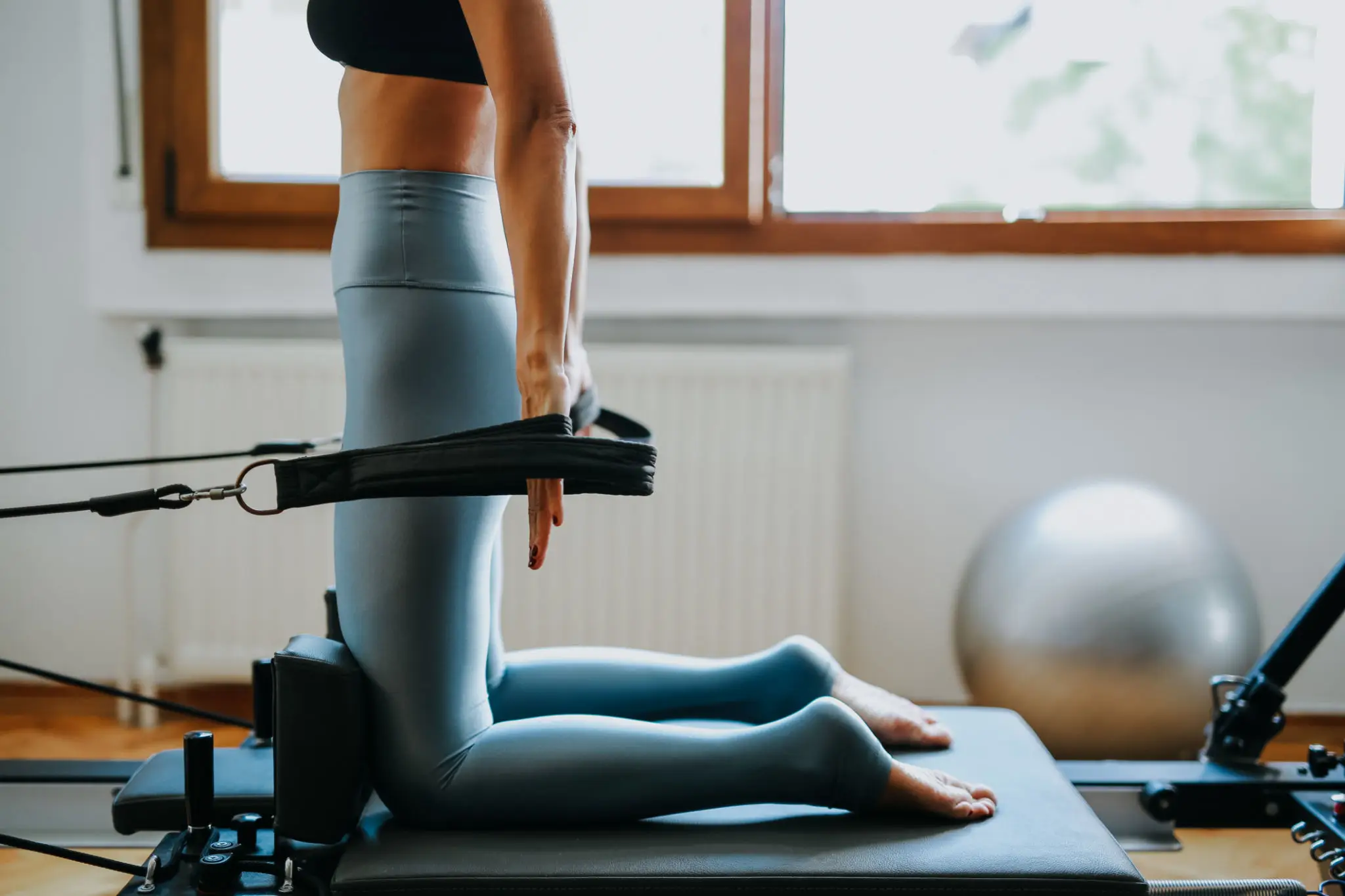 Person kneeling on a Pilates reformer for exercise.
