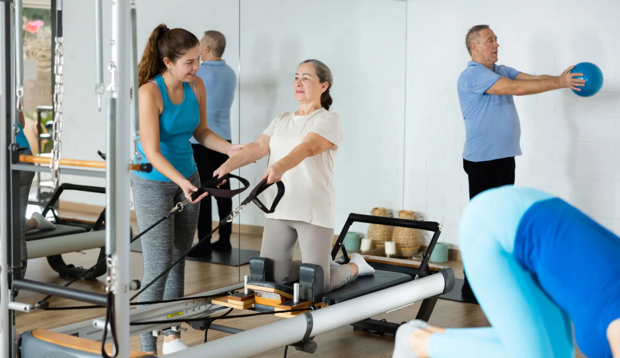 Two women exercising on Pilates reformers in a bright studio.