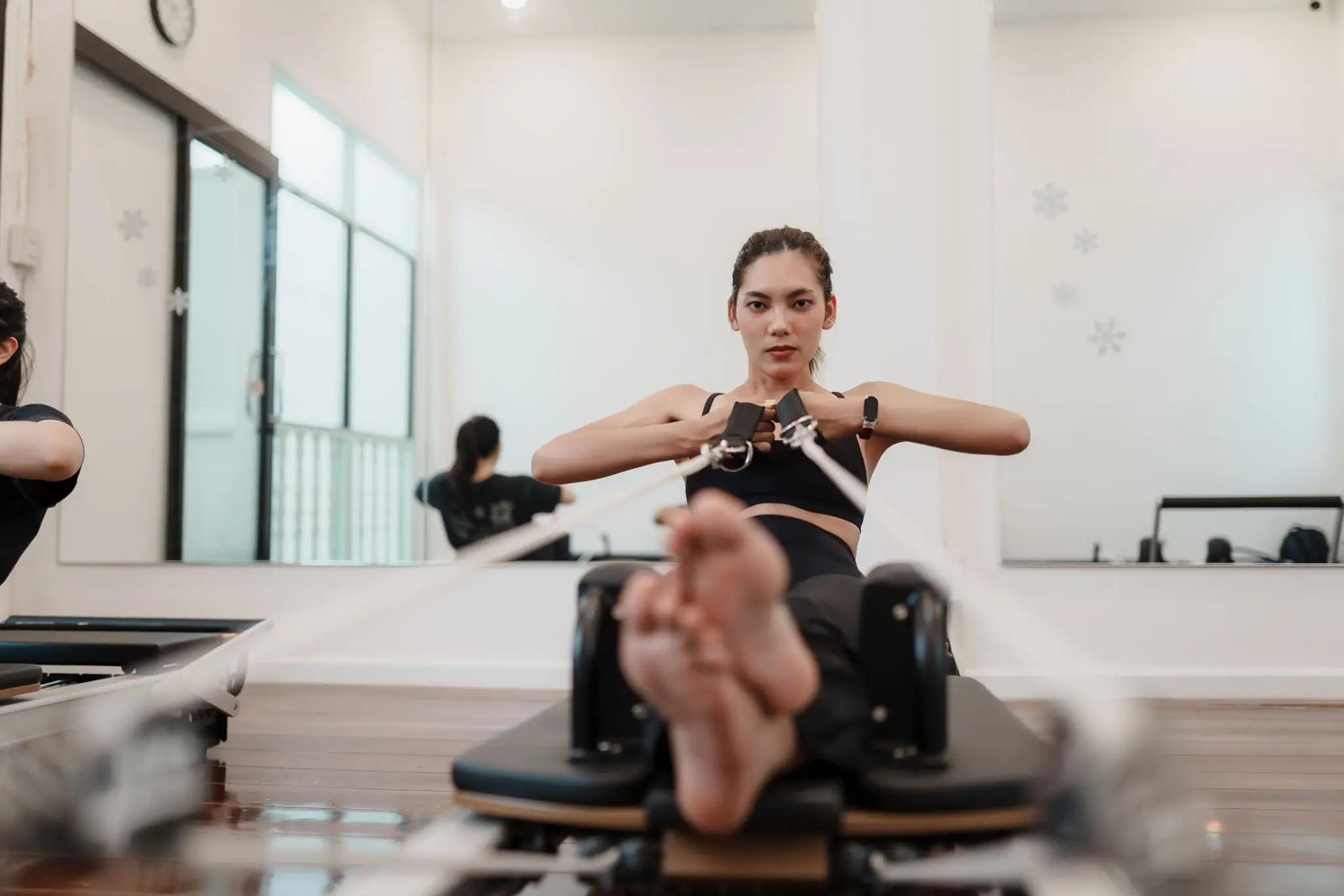 Woman exercising in a gym studio using a Pilates reformer machine.